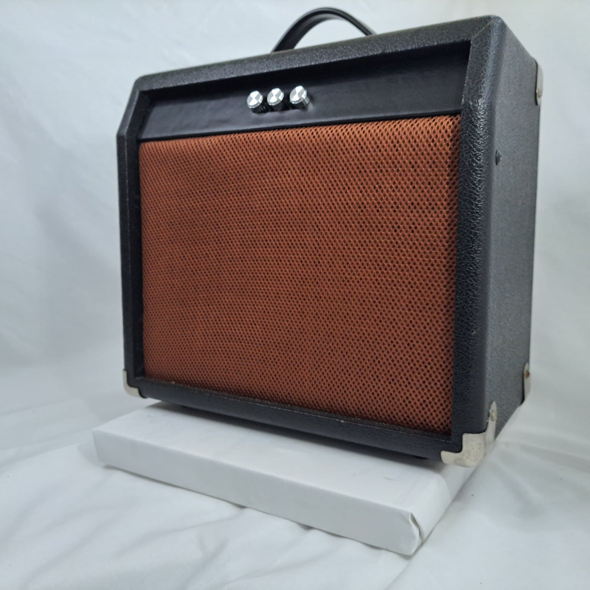 Small amplifier style speaker with a brown woven grille and a carry handle