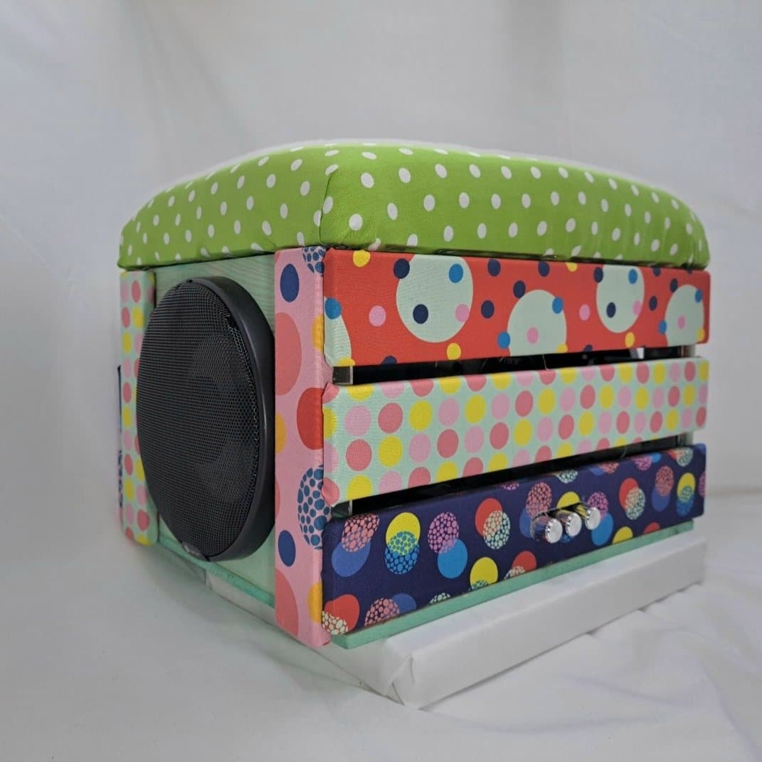 Cube speaker covered in polka dot fabric with a padded top