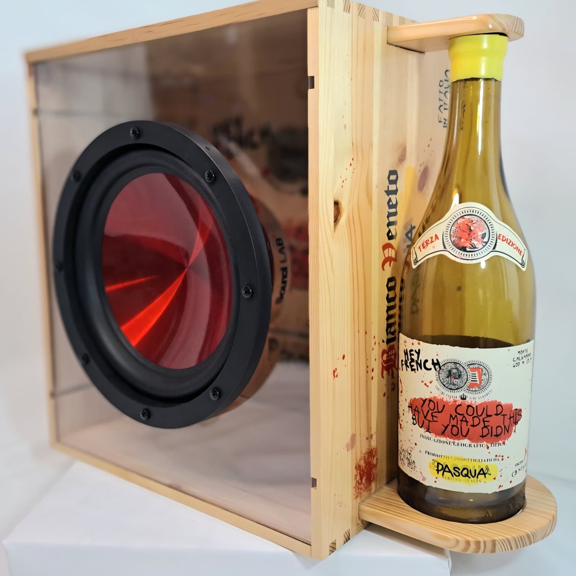Wine box speaker with a red cone driver behind a glass front, shown with a Pasqua bottle